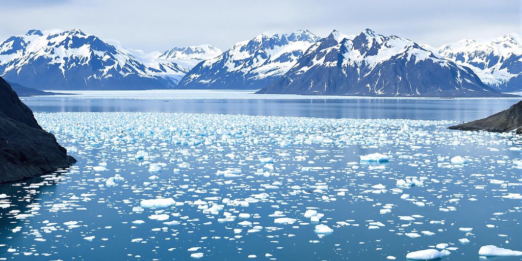 Kayakers in icy waters surrounded by mountains in Alaska.