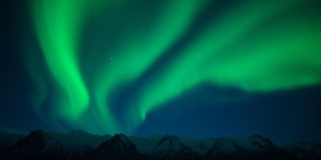 Green aurora ribbons dance above snow-covered Alaskan mountains.